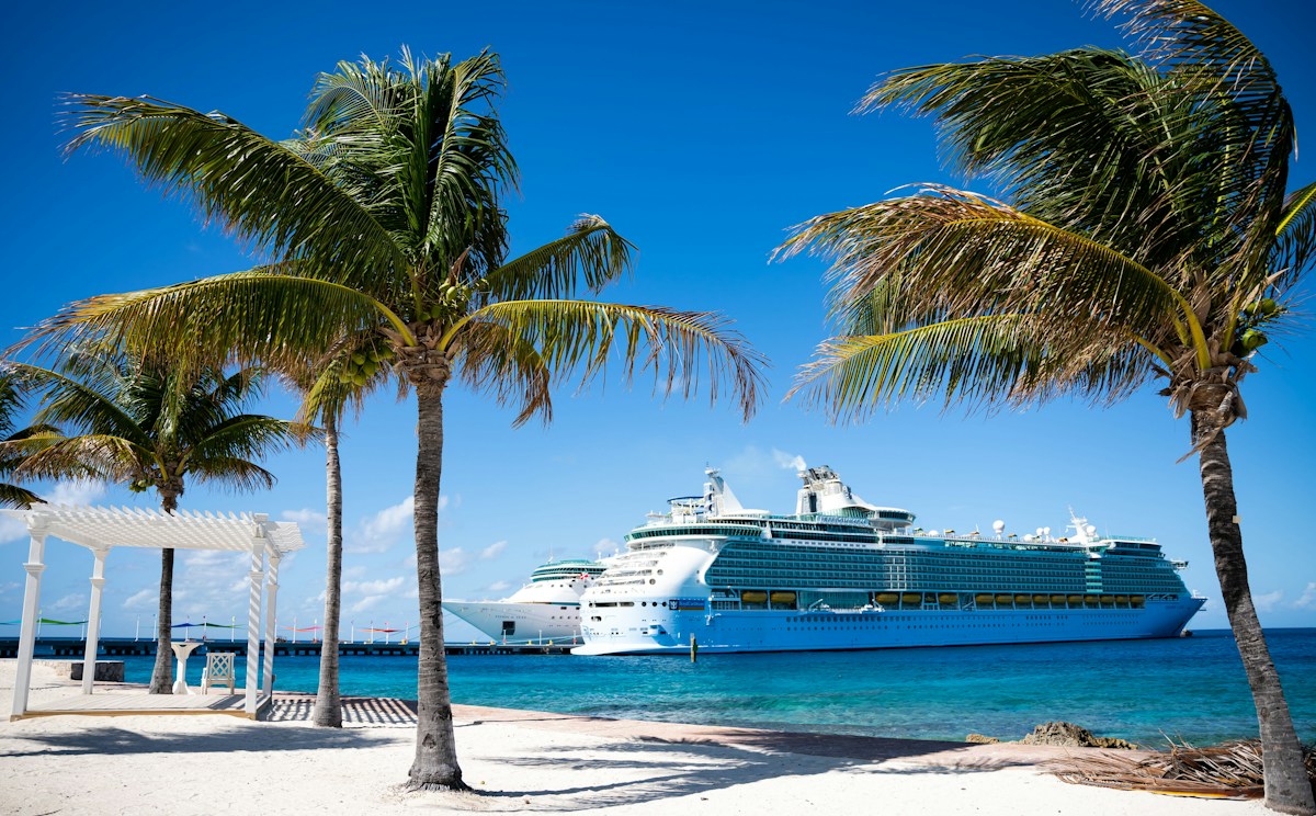 Cruise ships off a sunny Caribbean beach framed by palm trees